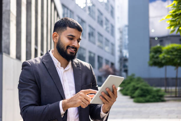 istock Smiling young Muslim male businessman using tablet while standing near office building, talking on video call 1862186632