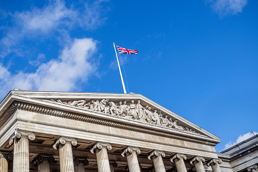 British Museum, London, England - November 7th 2023:  Facade of the British Museum with Union Jack against a blue sky