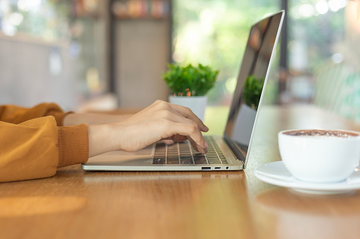 Woman hand working and typing on laptop keyboard on wood table