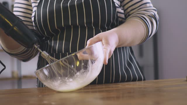 A woman beats egg whites with a mixer. Cooking sweets. Preparation for the holiday