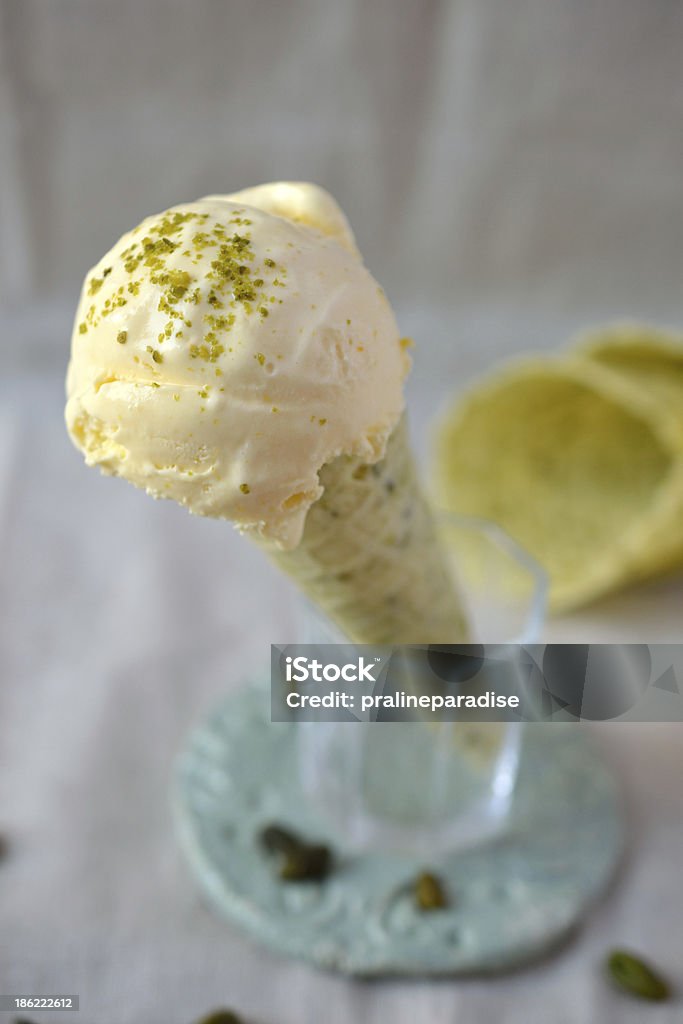 Orange ice cream in pistachio cone A scoop of orange ice cream in pistachio cone standing in a small glass on a greenish vintage clay plate. The scoop is sprinkled with ground pistachio. Two more empty pistachio cones can be found in the background. Dessert - Sweet Food Stock Photo