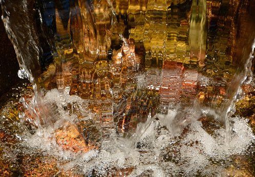 Fountain with golden color splashing water in a facet shape background. Abstract full frame picture.