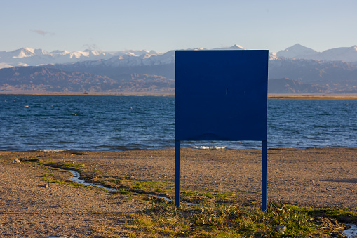 big blue sign on the beach of mountain lake at sunny afternoon