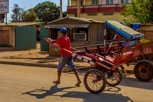 Ansirabe town, Madagascar, October 16, 2017: A rickshaw puller is seen pulling an empty Pulled rickshaw (pousse-pousse) on the street