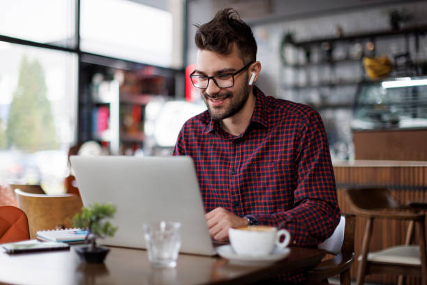 istock Smiling young man with headphones using laptop at a cafe 1862277855