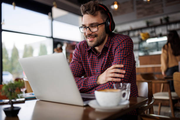 istock Smiling young man with headphones using laptop at a cafe 1862277866