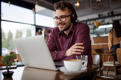 Smiling young man with headphones using laptop at a cafe
