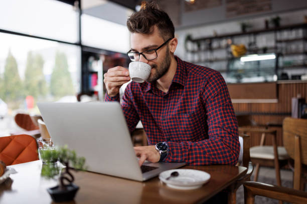 istock Smiling young man drinking coffee and using laptop at a cafe 1862277867