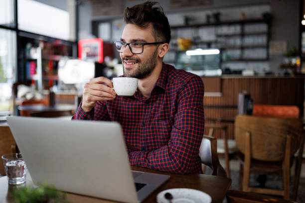 istock Smiling young man drinking coffee and using laptop at a cafe 1862277873