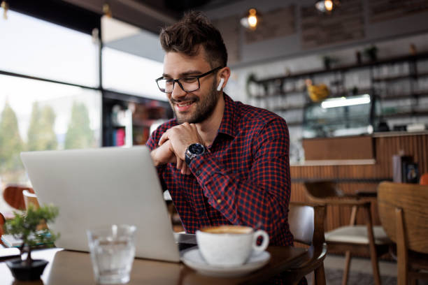 Smiling young man with headphones using laptop at a cafe