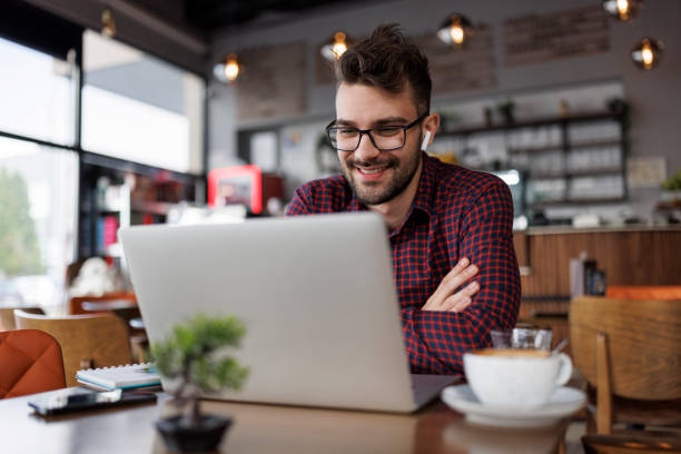 istock Smiling young man with headphones using laptop at a cafe 1862277890