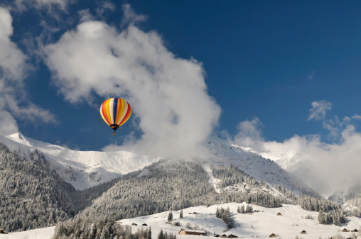 Colored hot-air balloon against blue sky with clouds. Snow-covered landscape in the Swiss Alps near Chateau-d'Oex.