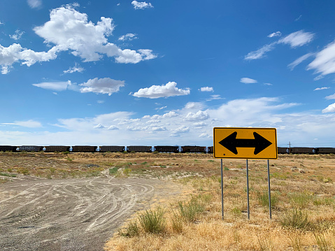 A mysterious sign indicating both ways with a freight train in the distance, in a wide open space.