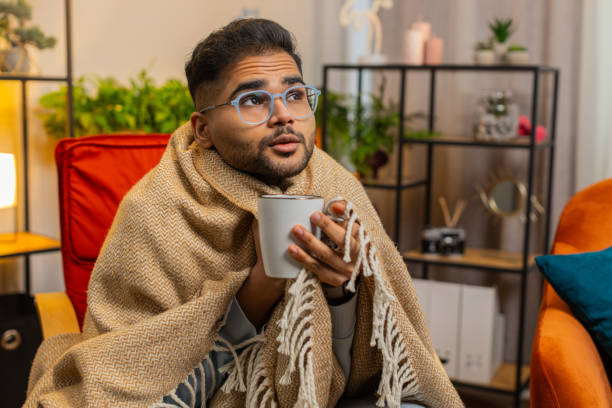 istock Sick Indian man wrapped in plaid sit alone shivering trembling from cold on chair drinking hot tea 1862311443