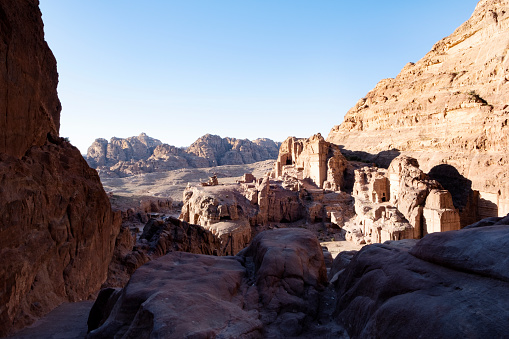 Looking out of a section of Petra and the mountains and desert in the distance. Petra is a world famous archeological site in Jordan. Petra is half-built, half-carved into the rock, and is surrounded by mountains riddled with passages and gorges. Also known as the \