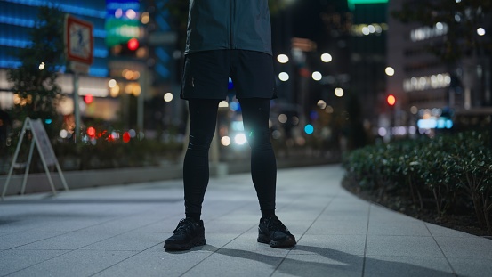 A male athlete is standing in the street at night.
