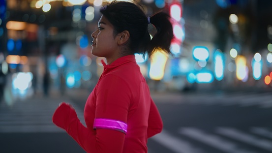 A multi-ethnic female athlete is running in a city at night.