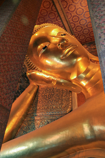 Huge golden reclining Buddha statue ans Thai art paint on the wall and pillar.