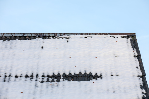 Melting snow on the slate roof of the house, blue sky.