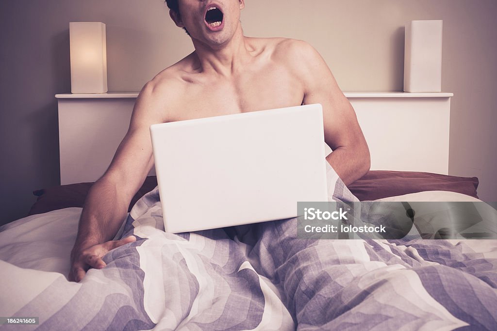 Young man in bed watching pornography on laptop Young naked man is sitting in a bed and watching pornography on his laptop Pornography Stock Photo