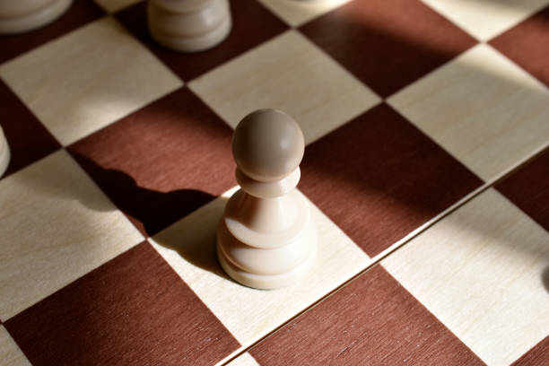 A close-up view of a wooden chess piece placed on a chessboard. The chess piece is in the foreground, showing details of its design. The background is blurred.