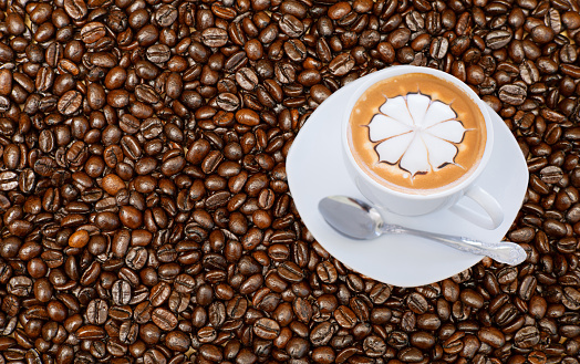 White coffee mug with floral pattern resting on ready-to-drink raw coffee beans, top corner photo.