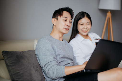 Smiling Asian Chinese couple using laptop at home. Online shopping and e-commerce concept.