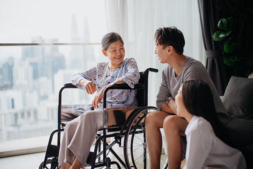 An Asian senior grandmother in wheelchair talking to her grandchildren at home