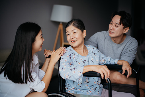 An Asian senior grandmother in wheelchair talking to her grandchildren at home