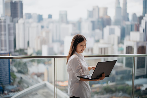 Young Asian woman working with laptop on the balcony of her apartment