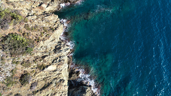 The aerial view showcases the rugged beauty of a rocky coastline meeting the clear sea.