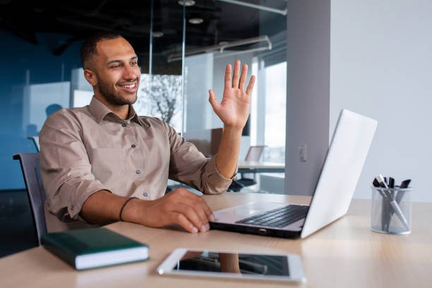 istock Happy successful and satisfied man talking on video call using laptop inside office, businessman waving hand smiling and greeting colleagues and partners, remote online meeting presentation 1862558593