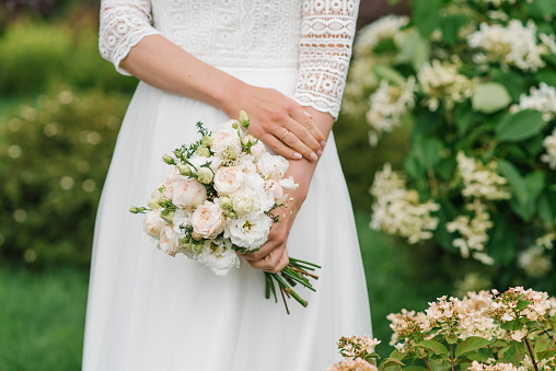 The bride holds a beautiful wedding bouquet of pink and white flowers in her hands