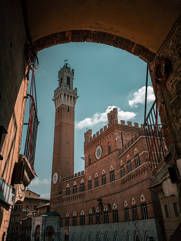 The Tower of Mangia (Torre del Mangia), against blue sky in bright sunlight in Campo Square (Piazza del Campo) in Siena, Tuscany, Italy
