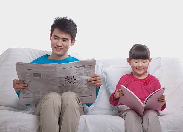 istock Father and daughter sitting on sofa reading separately, studio shot 186261574