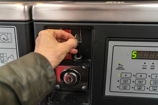 Female hand inserting a coin into the washing machine at  public laundromat service.