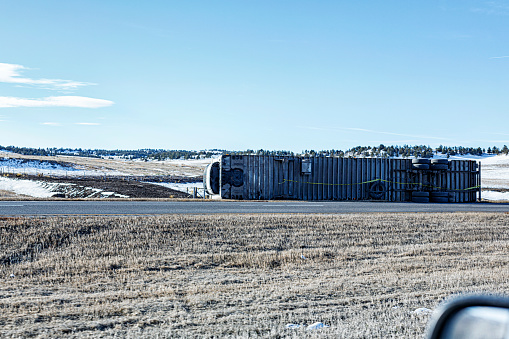 An overturned semi-truck container trailer lying on its side at the edge of the Interstate 80 expressway in Wyoming, USA - likely a victim of a truck driver's winter weather-related truck driving misfortune.