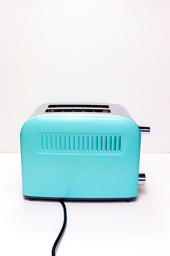 Whole grain bread roasted in vibrant retro style pastel coloured toaster machine close up