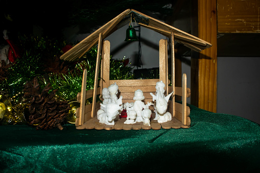 In the tranquil aura of a Yuletide evening, this evocative photograph showcases a beautifully arranged Christmas nativity scene, resting on a luscious green tablecloth that echoes the hues of everlasting life. The humble figurines are carefully crafted, with the Holy Family taking center stage, exuding a serene solemnity. Soft, ambient lighting casts a celestial glow upon the scene, highlighting the delicate textures and earthy colors of the statuettes. The wise men, shepherd, and angelic beings stand devotedly around, their silhouettes forming a poignant tableau that tells the timeless story of the birth of Jesus Christ. Behind the assembly, a rustic stable backdrop, reminiscent of that first holy night, completes the composition with a touch of divine simplicity. This image is not just a photograph but a capture of the essence of Christmas spirit, perfect for instilling a sense of peace and reverence during the holiday season