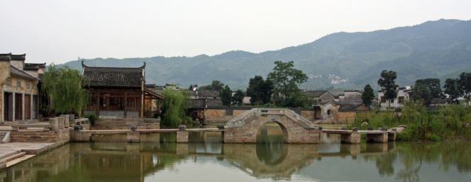 a picture of an ancient chinese town in anhui province - a pond and stone bridge in the foreground