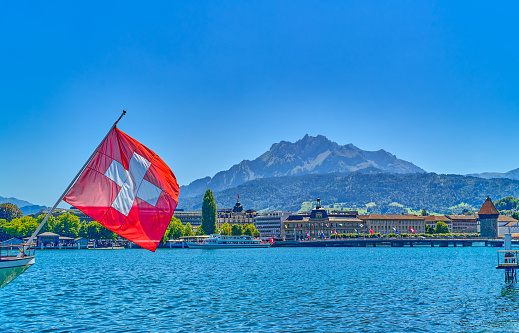 Lucerne, Switzerland, view of the city on the Reuss river with the Swiss flag on the left and the Pilatus mountain in the background