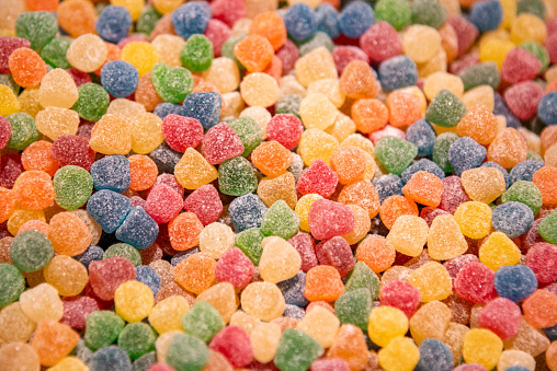 Group of small mixed colored chocolate coated candies in a transparent glass bowl on a table, isolated on white background, side view photo of yellow, orange, green, red and brown sweets