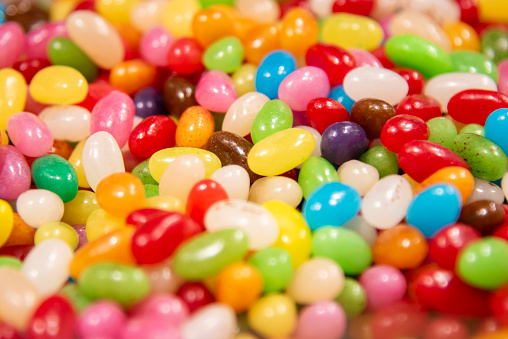 Top view of an assortment of multicolored candies, lollipops and jelly beans background. All the candies are at the center of the image making a horizontal stripe shape and leaving a useful copy space at the top and at the lower side of the image on a withe background.  Studio shot taken with Canon EOS 6D Mark II and Canon EF 24-105 mm f/4L