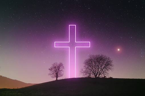 A large Christian cross neon at night on top of a hill