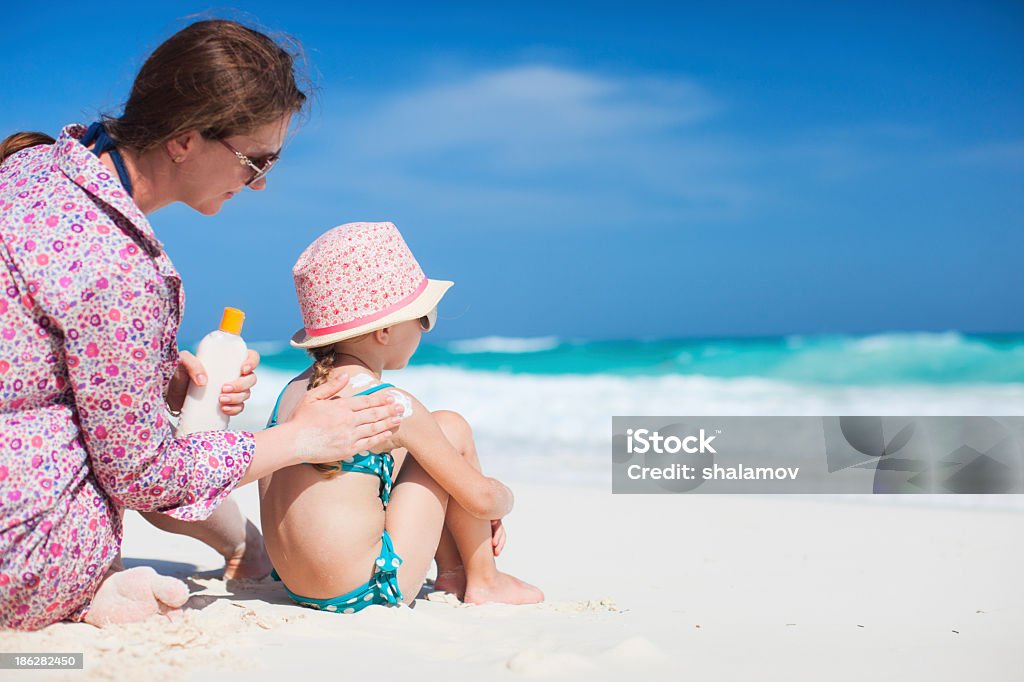 Mother putting sunscreen in her child on the beach Mother applying sunblock cream on her daughters shoulder Suntan Lotion Stock Photo