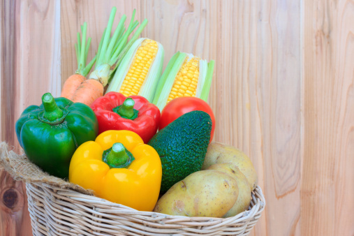 Fruits and vegetables in wicker basket on wood background