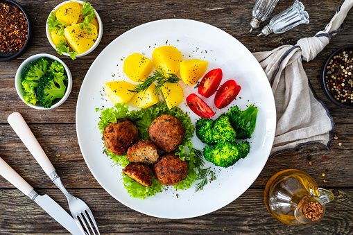 Roasted meatballs with boiled potato and cooked broccoli on wooden background