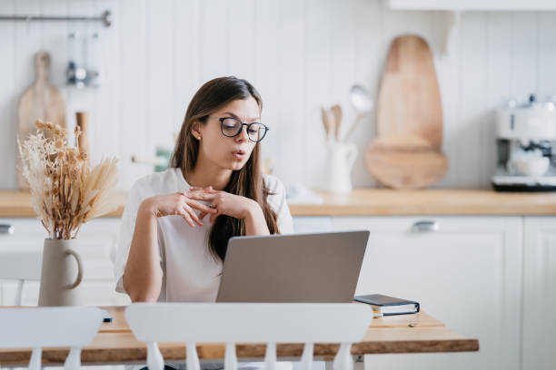 istock Focused young woman with glasses working on laptop at a minimalist kitchen table, her expression one of concentration and determination, surrounded by calm, neutral tones 1862849103