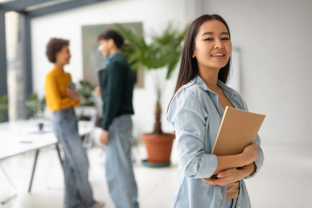 istock Happy asian student lady posing in university classroom and smiling at camera, classmates talking on background 1862898769