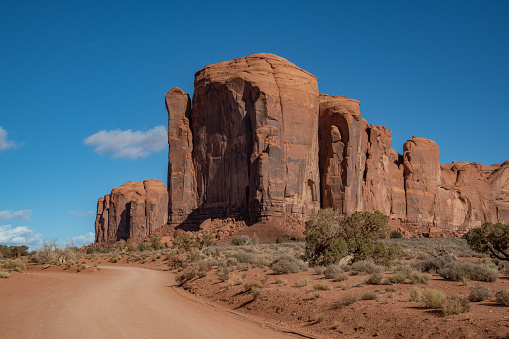 Dirt road through Tall spires and mesas of rich dark red rugged mountains near Monument Valley in Arizona and Utah of western USA in North America. This is part of the Navajo Nation in USA.  Nearest cities are Phoenix, Arizona, Salt Lake City, Utah, Denver and Durango, Colorado.